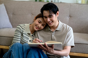 Asian adult couple reading book happily together in cozy home living room partners sharing quiet learning moment domestic lifestyle