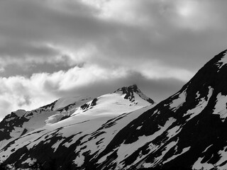 Dramatic mountain peak partially covered with snow under heavy clouds.