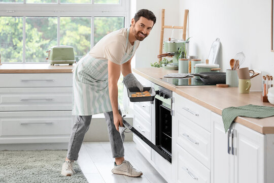 Young man with tasty cookies in baking pan near oven at home