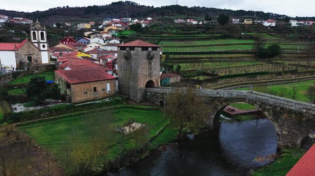 Ucanha village traditional homes, medieval stone bridge after sunset, terraced vineyards and wooded hills, drone shot