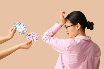 Young Asian woman suffering from headache and hands holding paper brains on beige background. Brain...