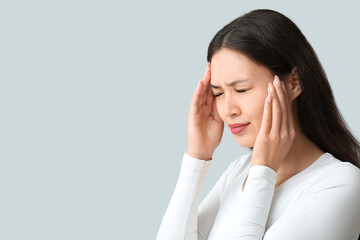 Young Asian woman suffering from headache on grey background. Brain Injury Awareness Month