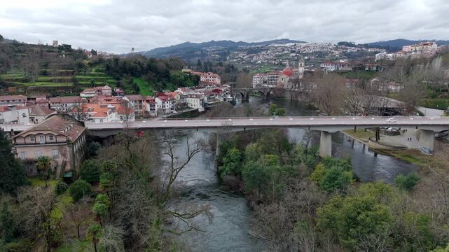 New bridge in Amarante city on Tamega riverbank featuring dense mixed autumn forest, Igreja de S&atilde;o Gon&ccedil;alo catholic church and historic stone bridge, Tracking drone shot