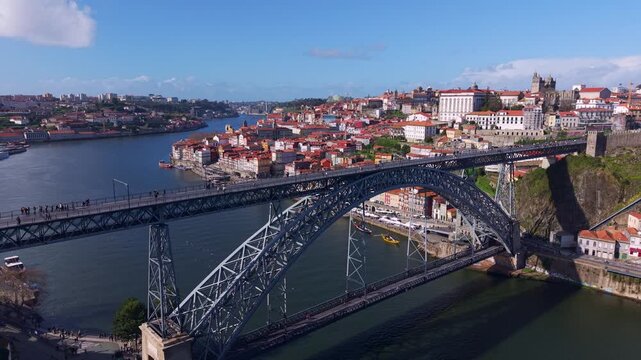 Drone shot of Luiz I bridge over river Douro with pedestrians and metro rail line at upper deck and public transportation road at lower deck, connecting Porto and Vila Nova de Gaia