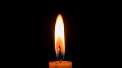 A single candle flame burns brightly with a warm glow in the darkness, symbolizing hope and peace.