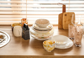 Many dirty dishes and glasses on wooden counter near window in kitchen