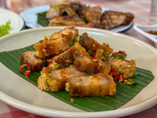 Fototapeta premium Stir fried pork belly with chili and salt is served on a banana leaf, presented as a ready to eat Thai dish on a restaurant table.