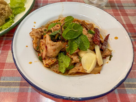 Nam tok pork is served with sliced meat chili herbs and mint. The Thai dish is ready to eat on a restaurant table.