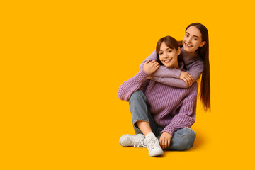 Fototapeta premium Beautiful young twin sisters hugging and sitting on yellow background