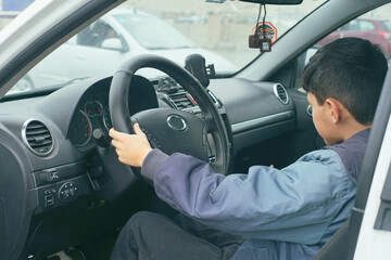 A young boy, engrossed in the act of pretending to drive, sits behind the steering wheel inside a parked car, seemingly lost in his imagination.