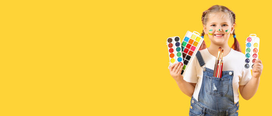 Little girl with paints on yellow background