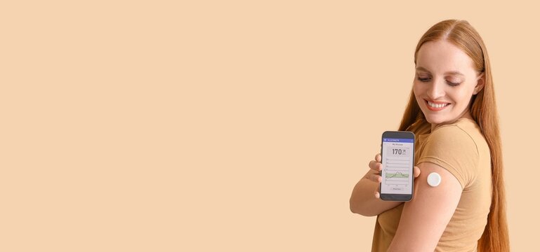 Woman with glucose sensor using mobile phone for measuring blood sugar level on beige background with space for text