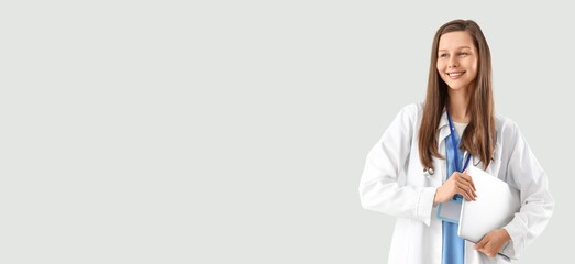 Female doctor holding laptop on light background with space for text