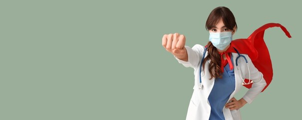Young female doctor in superhero costume on green background with space for text