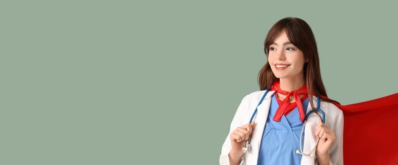 Young female doctor in superhero costume on green background with space for text