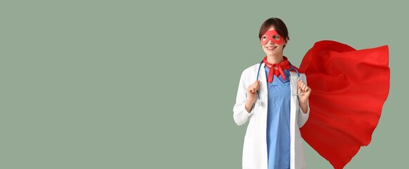 Young female doctor in superhero costume on green background with space for text