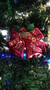 A glossy golden jingle bell decorated with a vibrant red bow and holly berries for holiday celebrations.