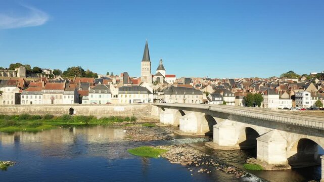 Scenic view of the historic stone bridge and charming old town of La Charite sur Loire under a clear blue sky. Picturesque French architecture lines the riverbank.