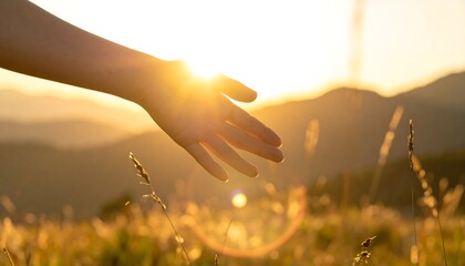 Hand reaching toward the sun over a golden field and mountains