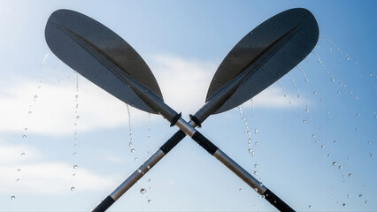 Friends joyfully laughing while rafting on a river, with oars dripping water against a clear blue sky background