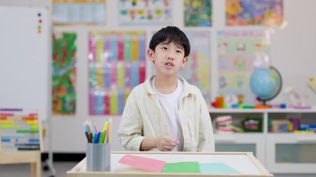 Asian schoolboy gesturing quiet sign in colorful classroom