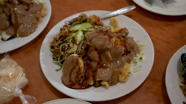Traditional Javanese lotek kupat dish with vegetables, rice cake and peanut sauce, establishing closeup