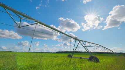 The irrigation system is operating in a lush green field that is situated beneath a bright sky