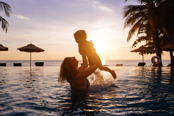 happy mother and child in swimming pool at sunset beach, family vacation