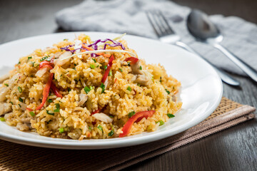 A white plate of stir-fried rice mixed with vegetables and meat, garnished with colorful toppings.