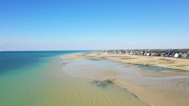 Wide aerial shot of Juno Beach at low tide with clear blue sky and coastal houses in Bernieres sur Mer, Normandy, France.