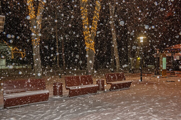 Empty park benches in the winter park during a strong snow fall at Christmas eve night.