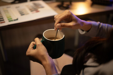 Close-up of hands stirring coffee in a mug, capturing a caffeine boost during a late-night work session