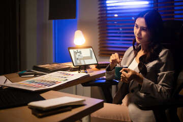 Asian interior designer enjoying caffeine during a late-night work session, focused on materials and design planning