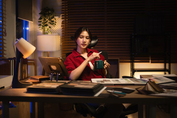 An Asian female interior designer focused on late night work at home, balancing creativity and caffeine with design catalogs on her desk