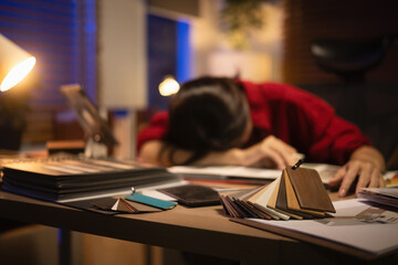 Creative interior designer asleep at desk after overtime, home office filled with selective focus on a sample boards and project documents