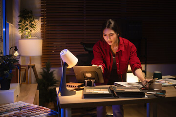 Focused interior designer working late at night, reviewing material samples and catalogs in a warm home office workspace