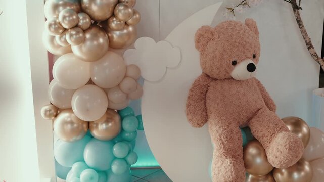 Plush teddy bear sitting on pastel balloon arrangement indoors