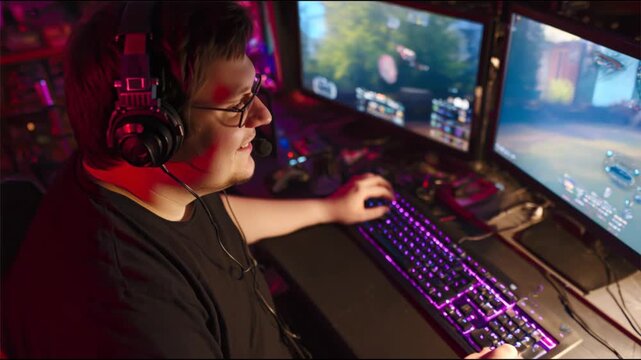 Young man wearing headset with microphone playing on a powerful personal computer with two monitors