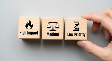 Hand arranging wooden blocks showing high impact, medium importance, and low priority concepts for task management.