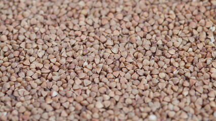 Fototapeta premium Groats texture in warm tone, Fresh buckwheat kernels scattered across surface, Detailed view of organic buckwheat kernels ideal for food photography and packaging design