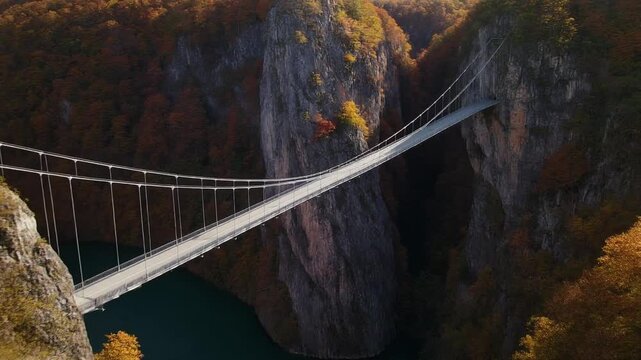 Majestic suspension bridge gracefully spanning a deep, rugged canyon with autumn foliage, showcasing a remarkable blend of human engineering and breathtaking natural landscape under a bright sky