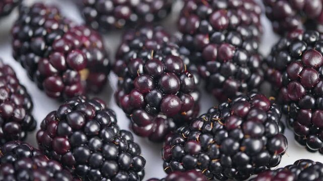 Clustered ripe blackberries on white background, Fresh ripe blackberries with reflective gloss and delicate drupelets on plain white backdrop for packaging or marketing