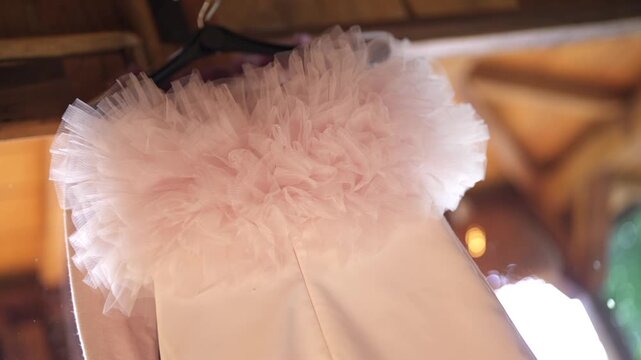 Slow motion establishing detail shot of layered tulle bodice hanging from bridal gown before wedding ceremony in warm ambient lighting.