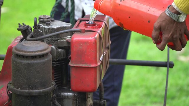 Macro shot of man filling in petrol, diesel, kerosene fossil fuel into a generator engine agriculture farming machine from a red can showing the continued reliance on these old forms of energy.