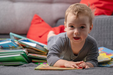 Toddler sitting among books, representing early intellectual curiosity and joyful learning in a cozy home environment. Copy space for text or design.
