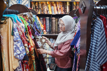 Fototapeta premium Asian woman shopping for traditional Indonesian batik garments in a fashion store.