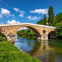 Obraz premium A stone arch bridge spans a river, lush greenery on its banks