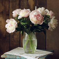 Peonies bouquet in glass vase on rustic wood background