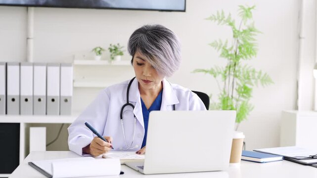 Doctor looking at laptop screen writing in notebook for research planning or medical tech innovation in hospital office. Healthcare medic worker, research strategy book notes and online communication.