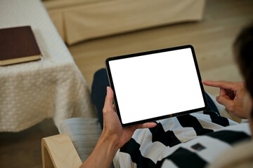 Close up view of a man using blank screen digital tablet on armchair